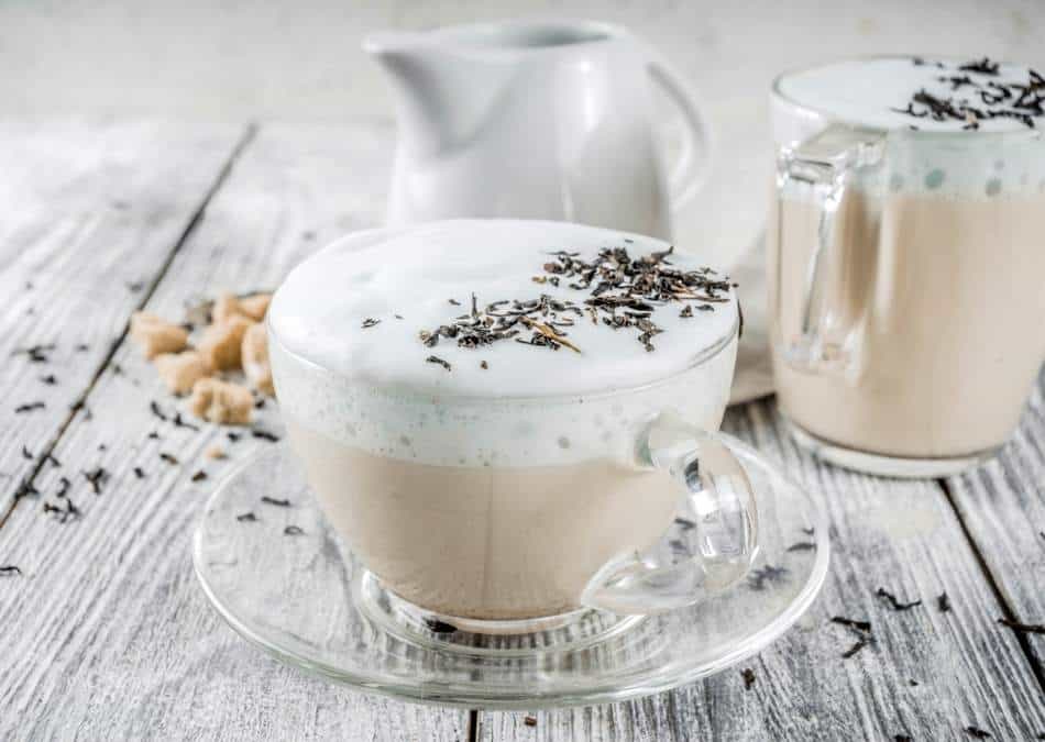 london fog tea latte in a glass cup and saucer with dried lavender flowers sprinkled on top